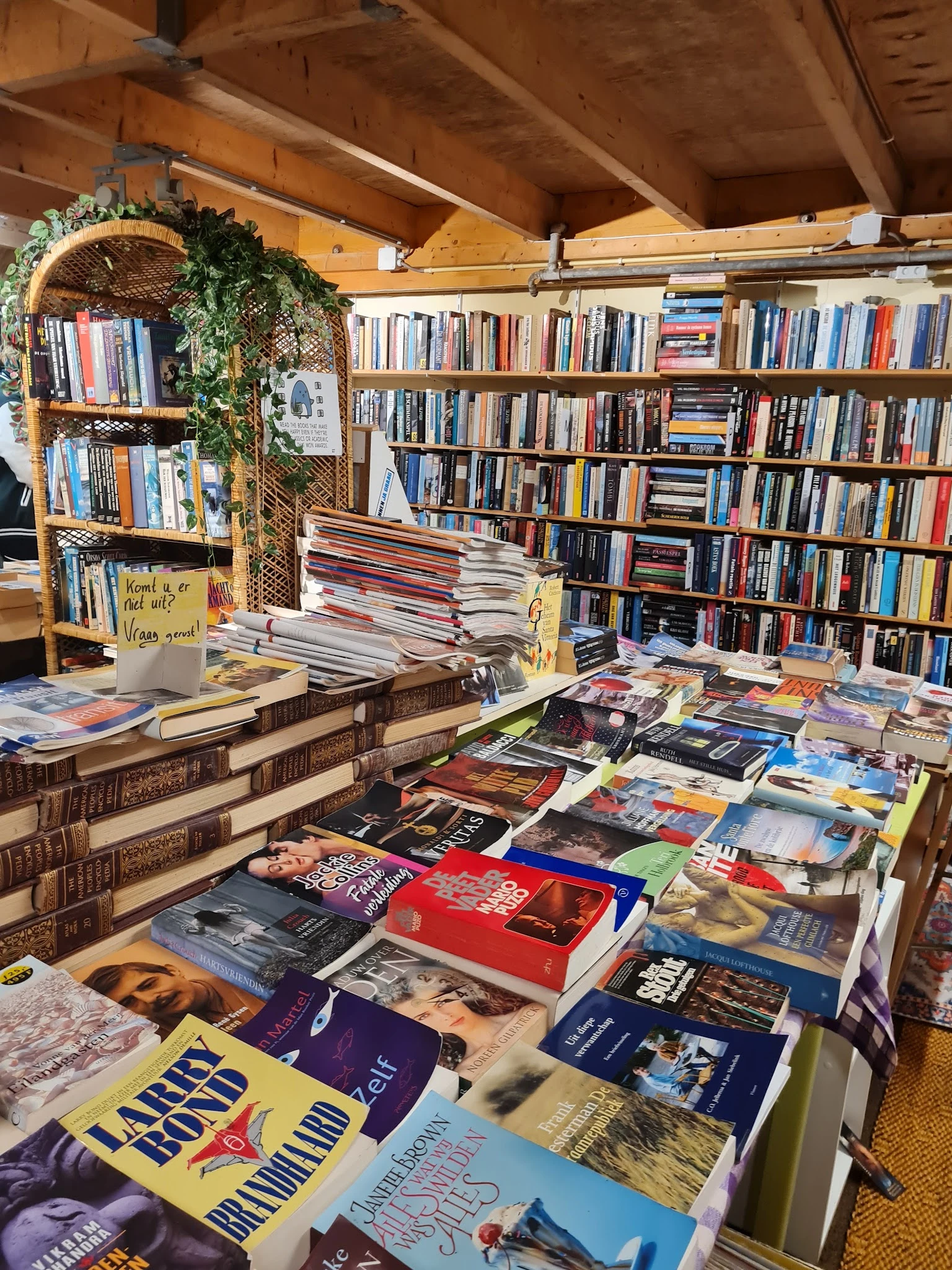 Uitgestalde tweedehands boeken op de vloer en tafels, met boekenkasten vol boeken op de achtergrond