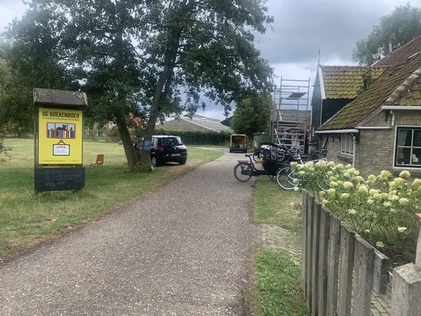 Ingang van kringloopwinkel met gele brievenbus, grindpad, fietsen en stenen gebouw met aangepaste dak