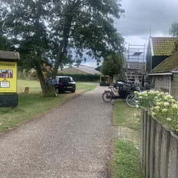 Ingang van kringloopwinkel met gele brievenbus, grindpad, fietsen en stenen gebouw met aangepaste dak