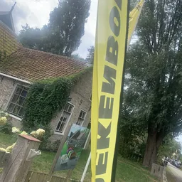 Voorkant van stenen woning met klimop en geel bedrijfsbord