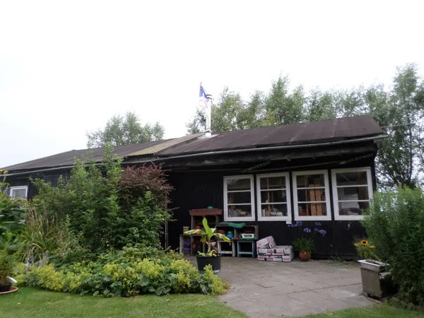 Voorgevel van een donkere houten kringloopwinkel met witte ramen en een overdekt terras met tuinmeubelen