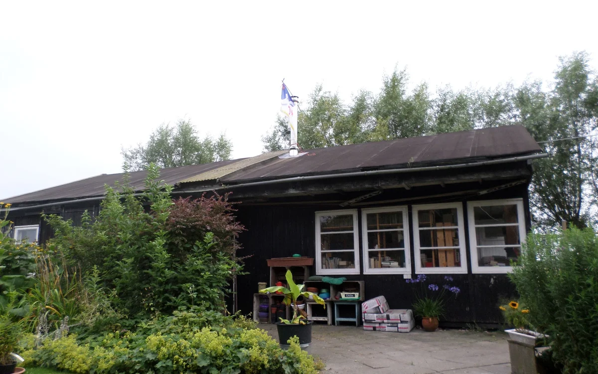Voorgevel van een donkere houten kringloopwinkel met witte ramen en een overdekt terras met tuinmeubelen