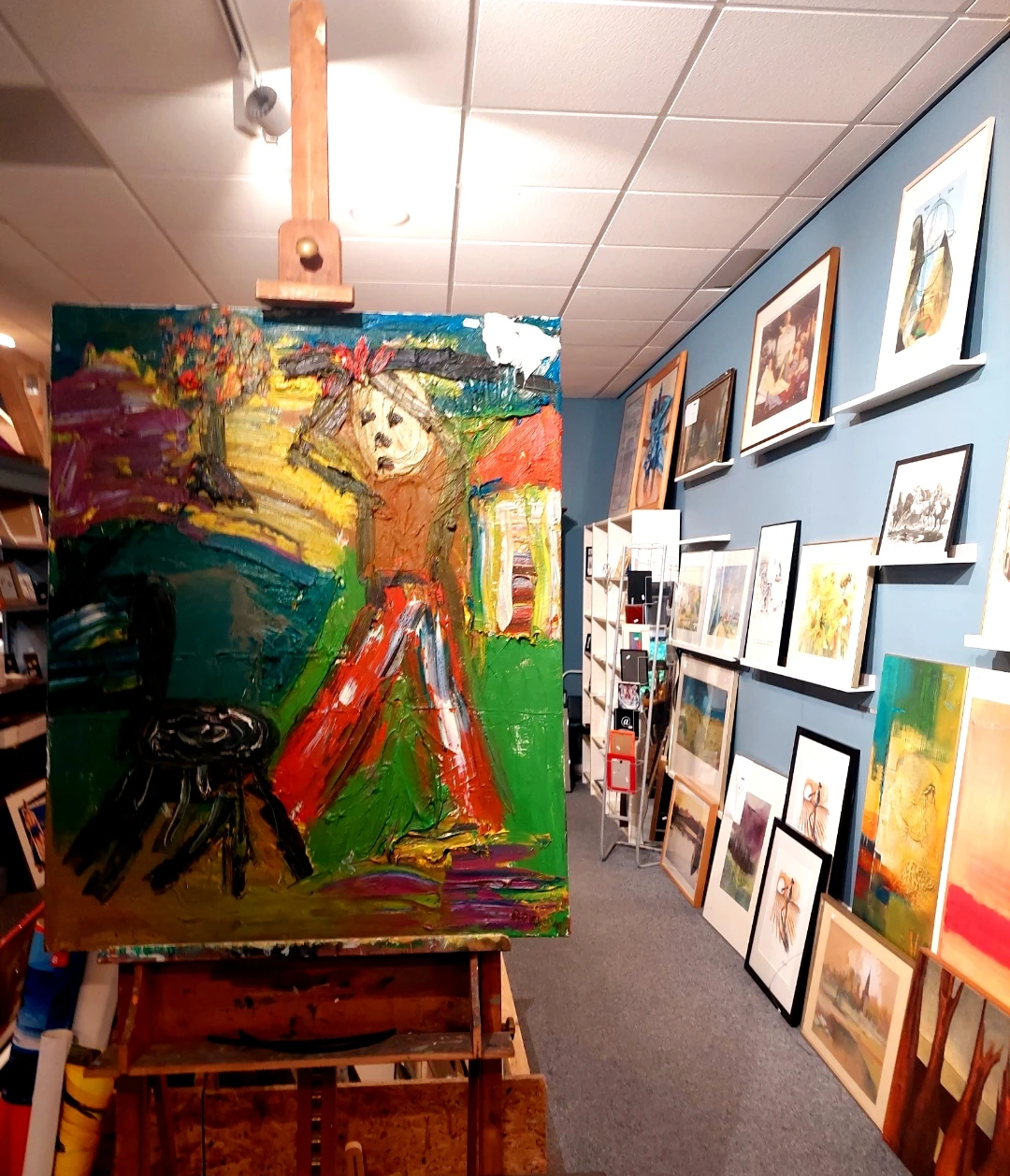 Winkelinterieur met kunstwerken aan muren en een groot kleurrijk schilderij op ezel