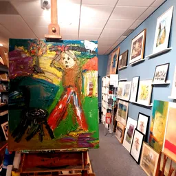 Winkelinterieur met kunstwerken aan muren en een groot kleurrijk schilderij op ezel