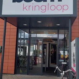 Glazen pui van kringloopwinkel met zwart frame en ingang, rode bakstenen gevel