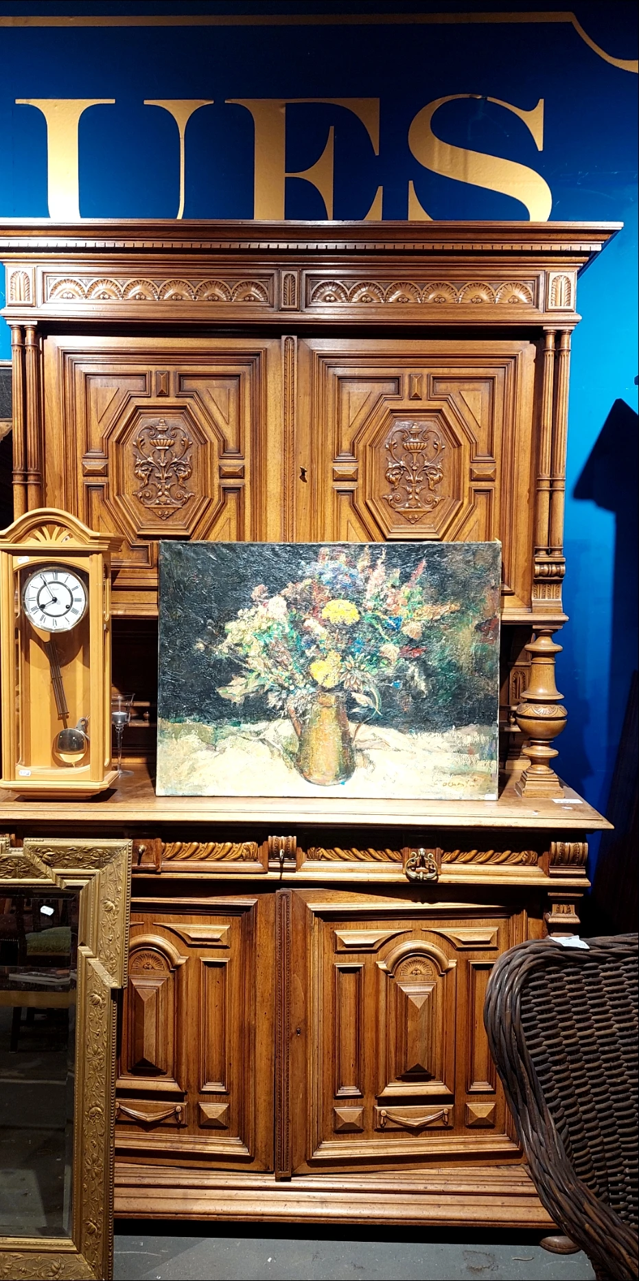 Schilderij met bloemen in vaas tegen donkere achtergrond, geplaatst tegen houten wand met wandklok