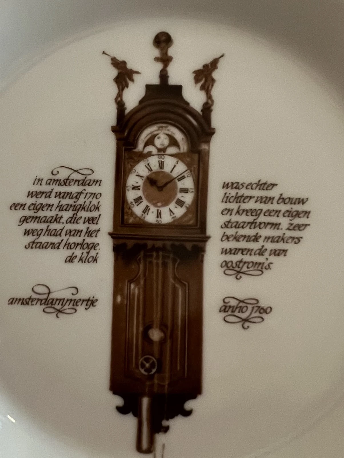 Staande klok met houten kast en wijzerplaat met Romeinse cijfers, versierd met Nederlandse teksten op de muur