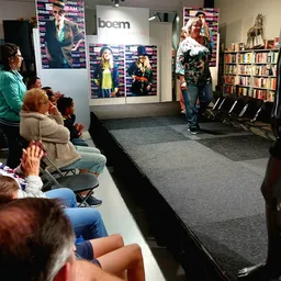 Publiek zit op stoelen en kijkt naar een presentatie of event op een podium in de winkel