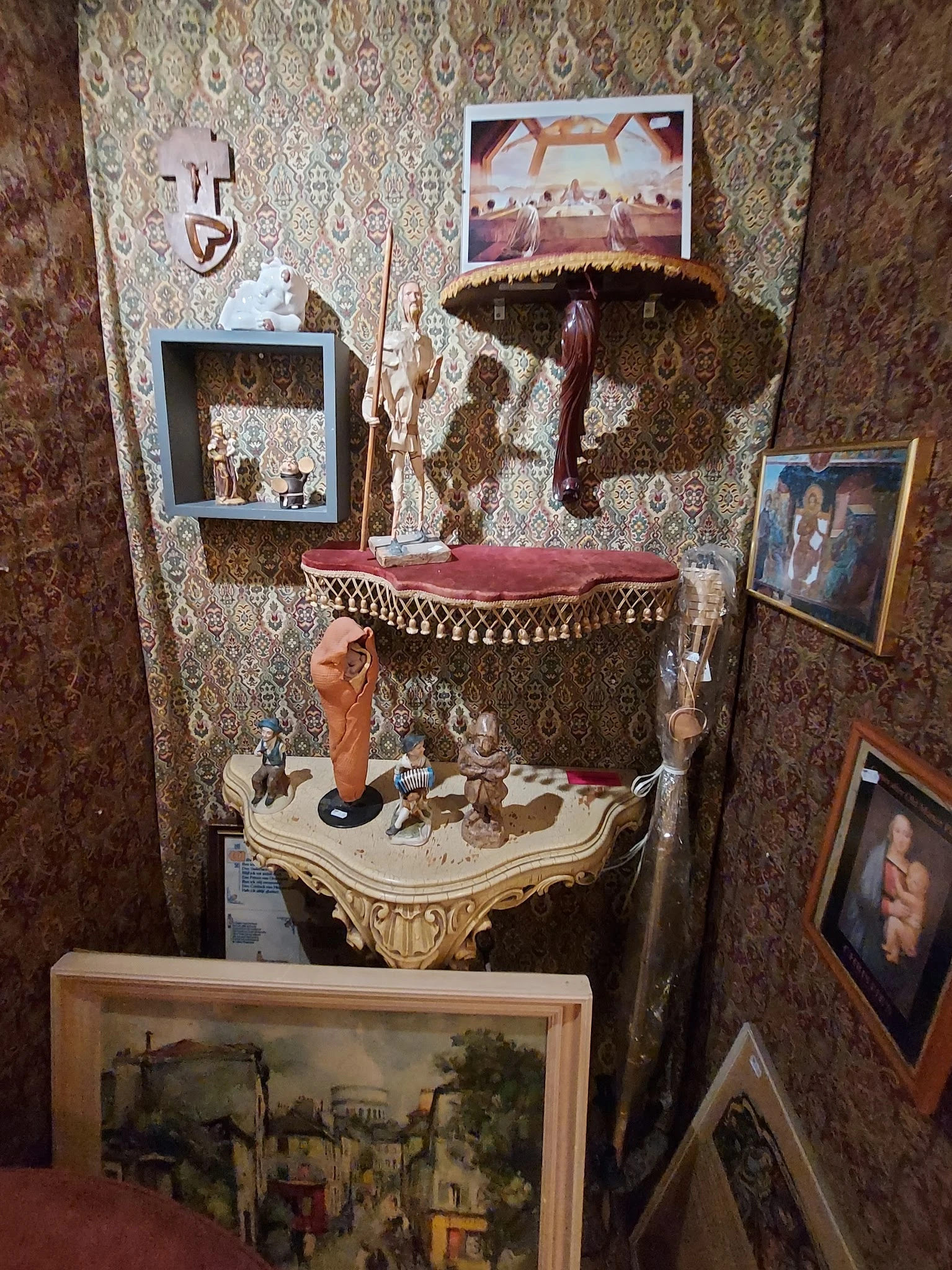 Vintage decoratieve tafel met gouden ornamenten en verzameling beeldjes, tegen behangen muur met framed foto's