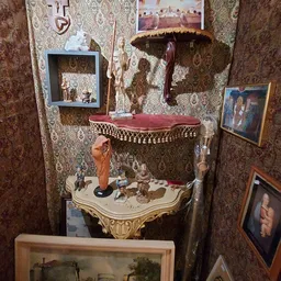 Vintage decoratieve tafel met gouden ornamenten en verzameling beeldjes, tegen behangen muur met framed foto's