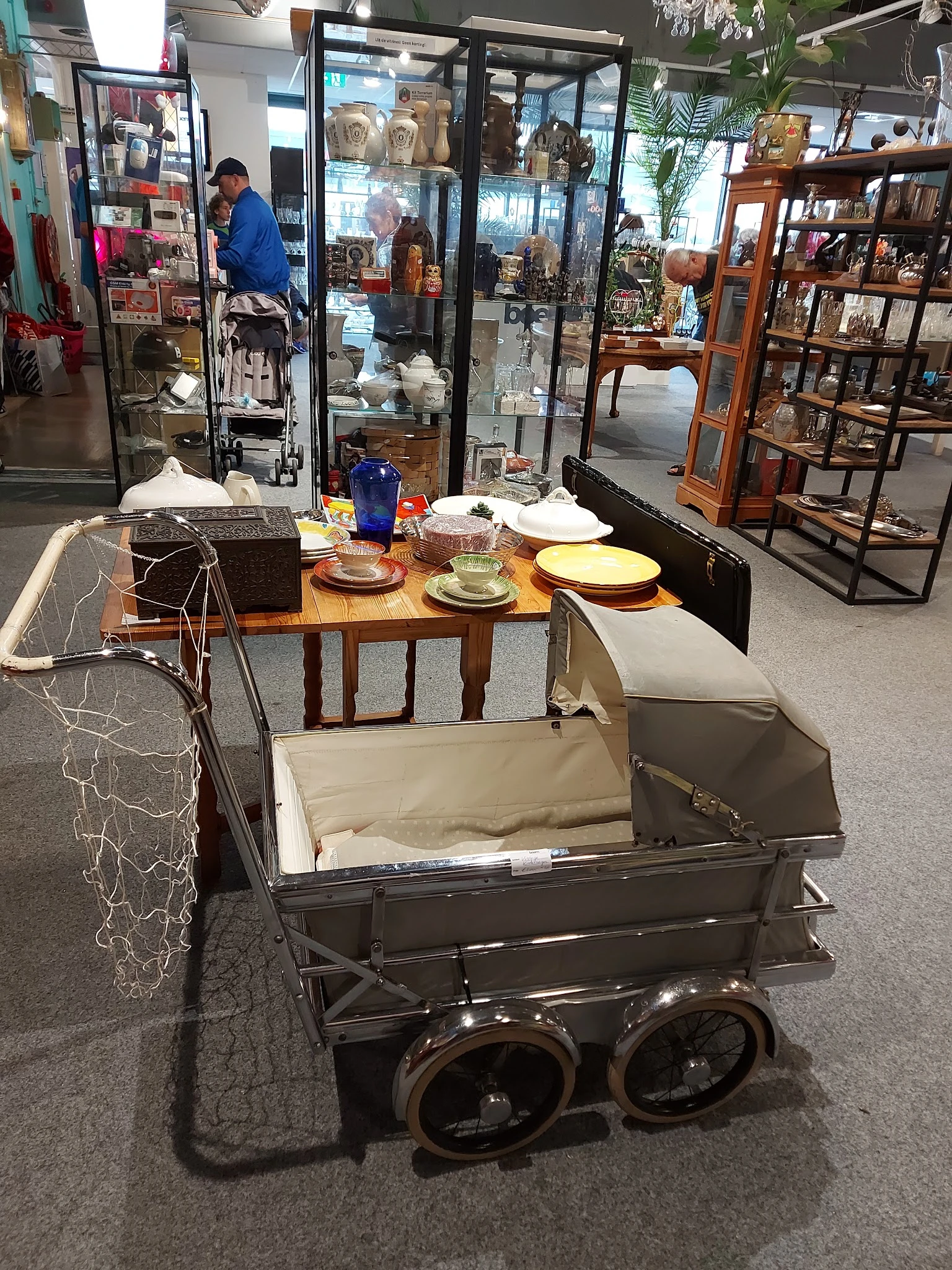 Uitgestalde serviesgoed, een kinderwagen en diverse huishoudelijke artikelen in de winkel