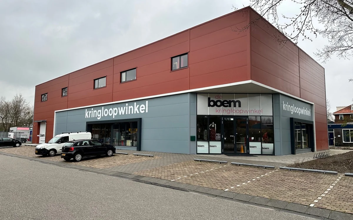 Moderne kringloopwinkel met rood-bruine bovengevel en blauwe winkelpui, parkeerplaats vooraan