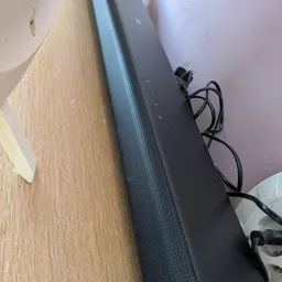 Zwarte soundbar of luidspreker met stroomkabel op houten vloer