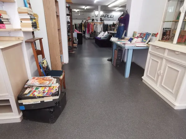 Winkelvloer van kringloopwinkel met stellingen, kleding aan hangers, boeken en diverse spullen uitgestald