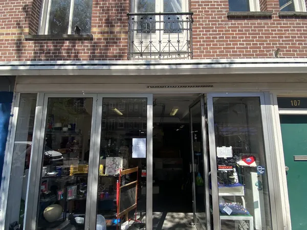 Winkelpui van kringloopwinkel met grote ramen, zichtbaar aanbod van spullen binnen, bakstenen gevel boven