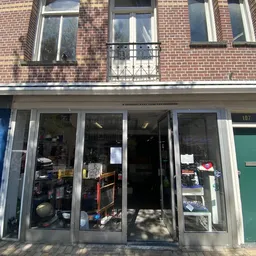 Winkelpui van kringloopwinkel met grote ramen, zichtbaar aanbod van spullen binnen, bakstenen gevel boven
