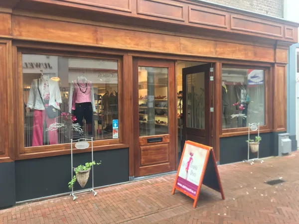 Houten gevel van kringloopwinkel met etalages met dameskleding, rode stormbord op straat