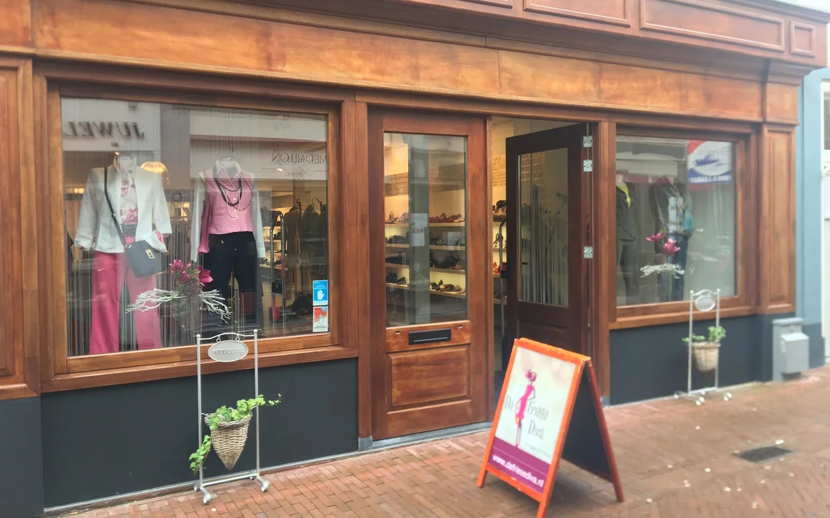 Houten gevel van kringloopwinkel met etalages met dameskleding, rode stormbord op straat