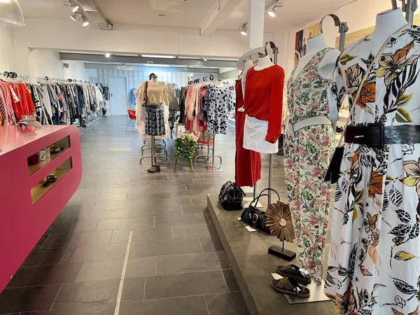 Winkelinterieur met kledingrekken, mannequins in rode en bloemenprint jurken, roze kast en zwarte accessoires