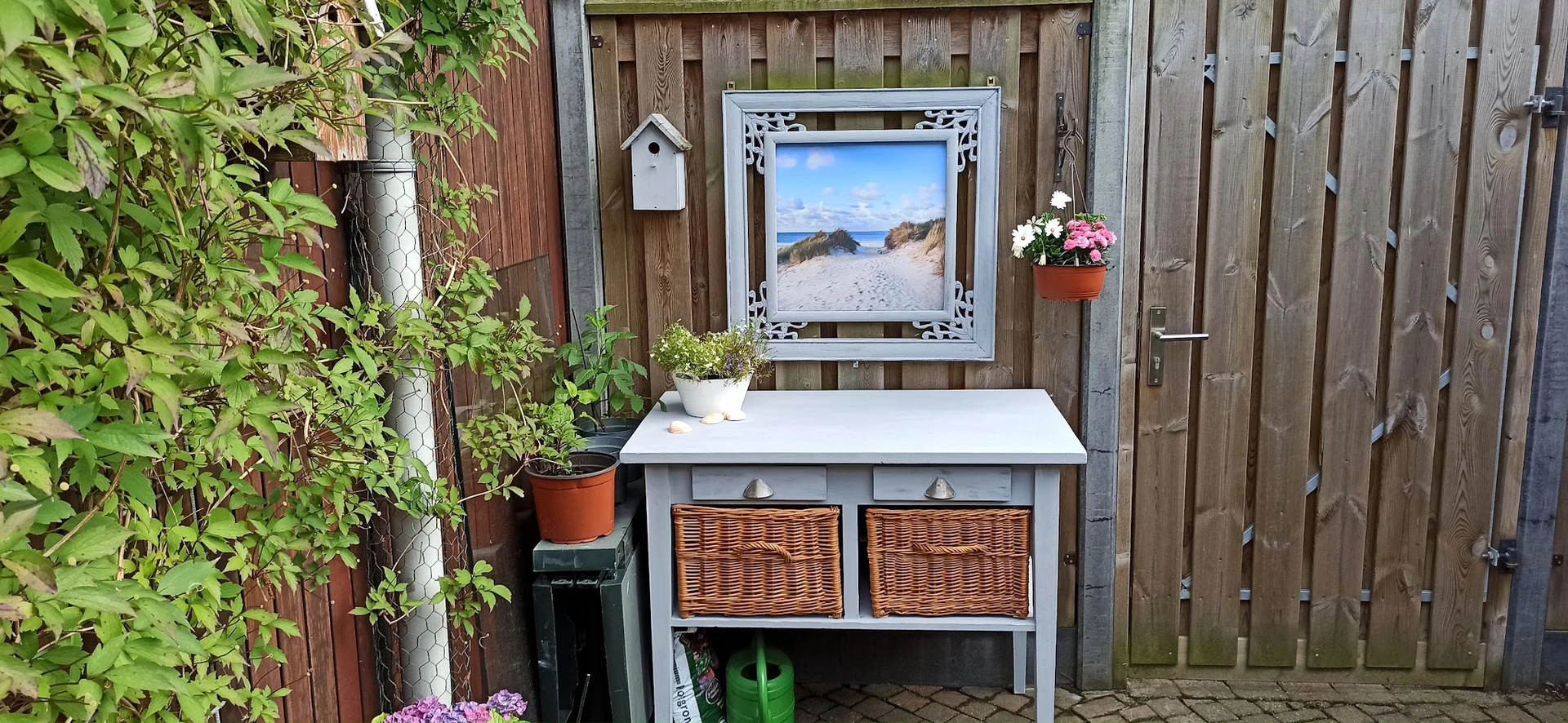 Wit tuinmeubel met wichelmatten en een strandafbeelding aan de achterwand in een tuin