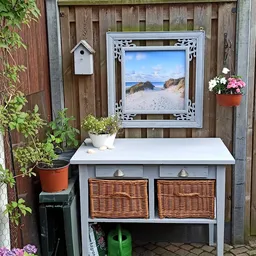 Wit tuinmeubel met wichelmatten en een strandafbeelding aan de achterwand in een tuin