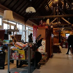 Ruim interieur van kringloopwinkel met diverse meubelen, boeken, decoratiespullen en klanten die aan het winkelen zijn