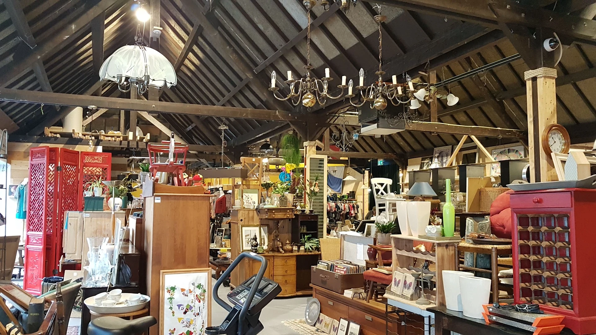 Ruim interieur van kringloopwinkel met houten meubels, lampen, boekenkasten en diversen huishoudelijke artikelen onder een ge