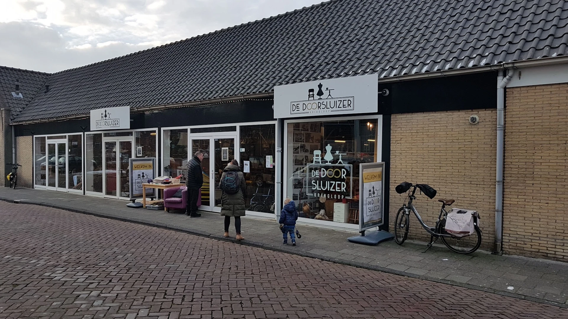 Gevel van kringloopwinkel De Doorsluizer met etalage, ingang en fiets ernaast