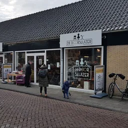 Gevel van kringloopwinkel De Doorsluizer met etalage, ingang en fiets ernaast