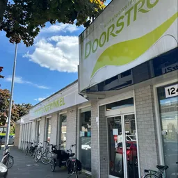 Grijze bakstenen gevel van kringloopwinkel met groene logo en etalageruiten, fietsen geparkeerd ernaast