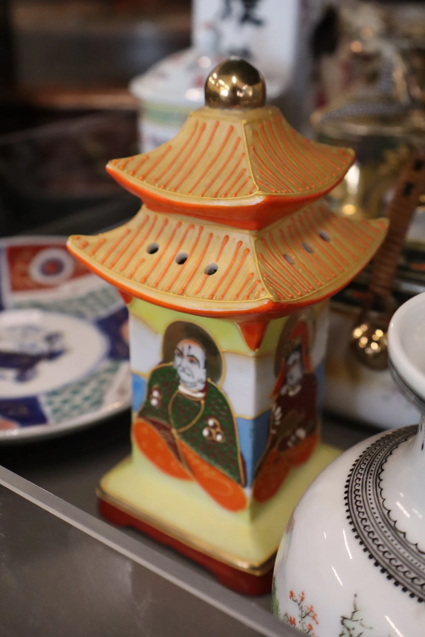 Decoratief Aziatisch porseleinenhuisje met oranje dak en figuren, tussen serviesgoed op display