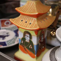 Decoratief Aziatisch porseleinenhuisje met oranje dak en figuren, tussen serviesgoed op display