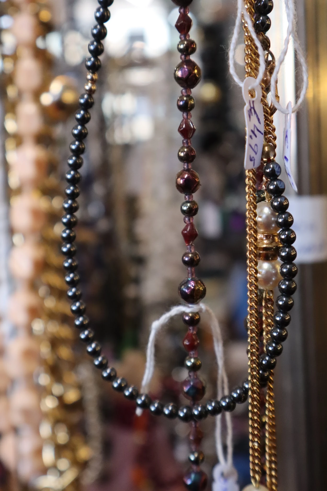 Close-up van hangende sieraden met parels en kralen in verschillende kleuren: zilver, goud en rood.