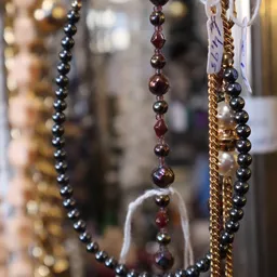 Close-up van hangende sieraden met parels en kralen in verschillende kleuren: zilver, goud en rood.