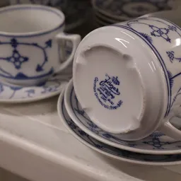 Close-up van een wit porseleinen kopje met blauw decoratief patroon en fabrikantsmerk op de bodem