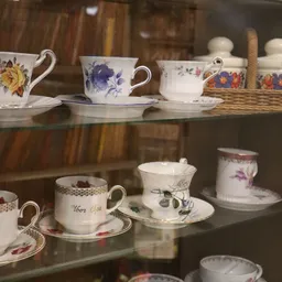 Vitrinekast met antiek porselein servies, kopjes met bloemmotieven en gouden accenten