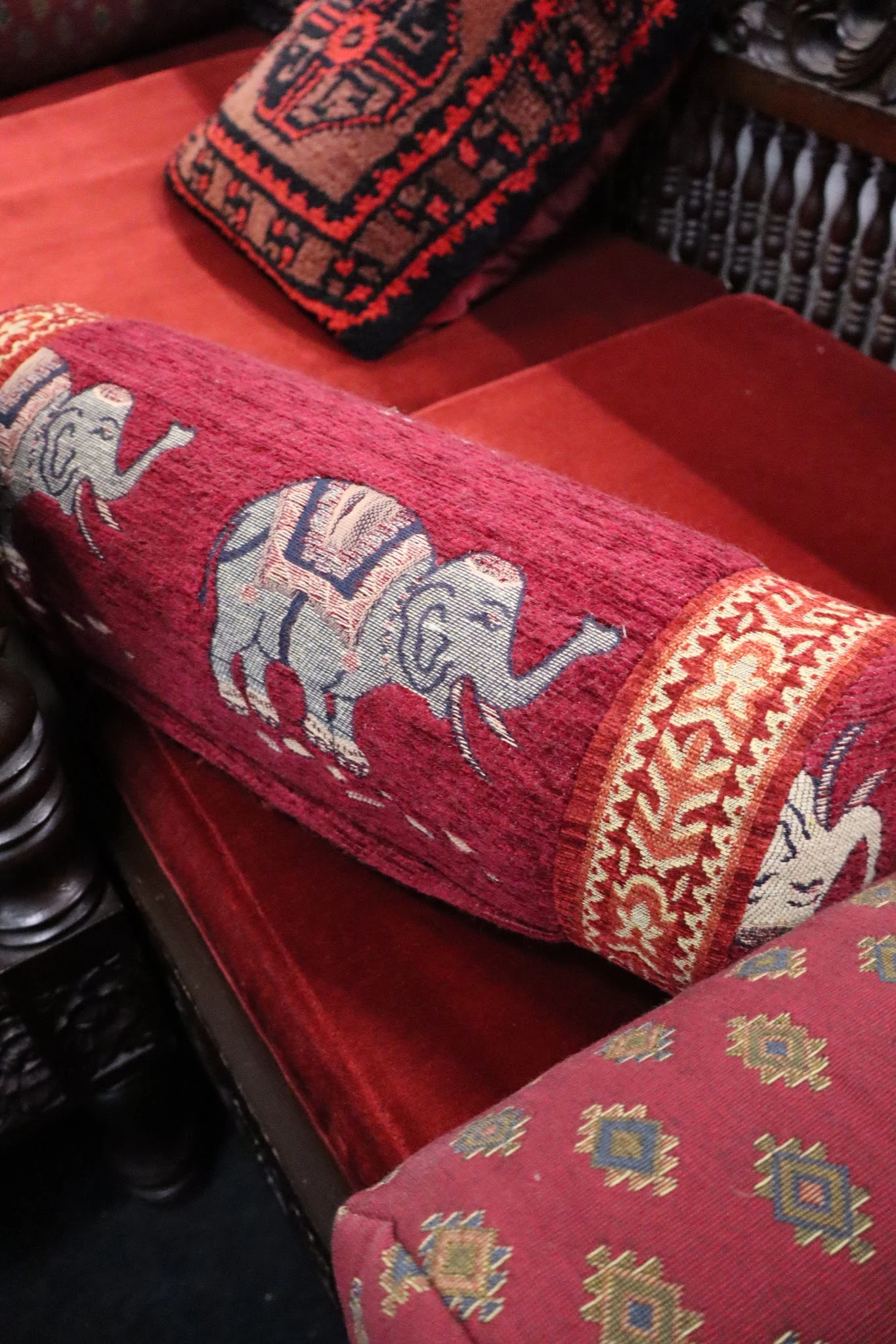 Close-up van een rood/bordeaux textiel met traditionele olifantenmotieven en decoratieve rand