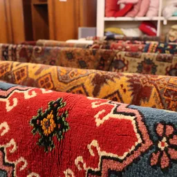 Stapel traditionele handgeknoopte tapijten met diverse kleurige patronen in rood, geel en blauw