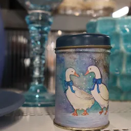 Close-up van een decoratief blikje met twee witte eenden met blauwe strikjes op grijze achtergrond