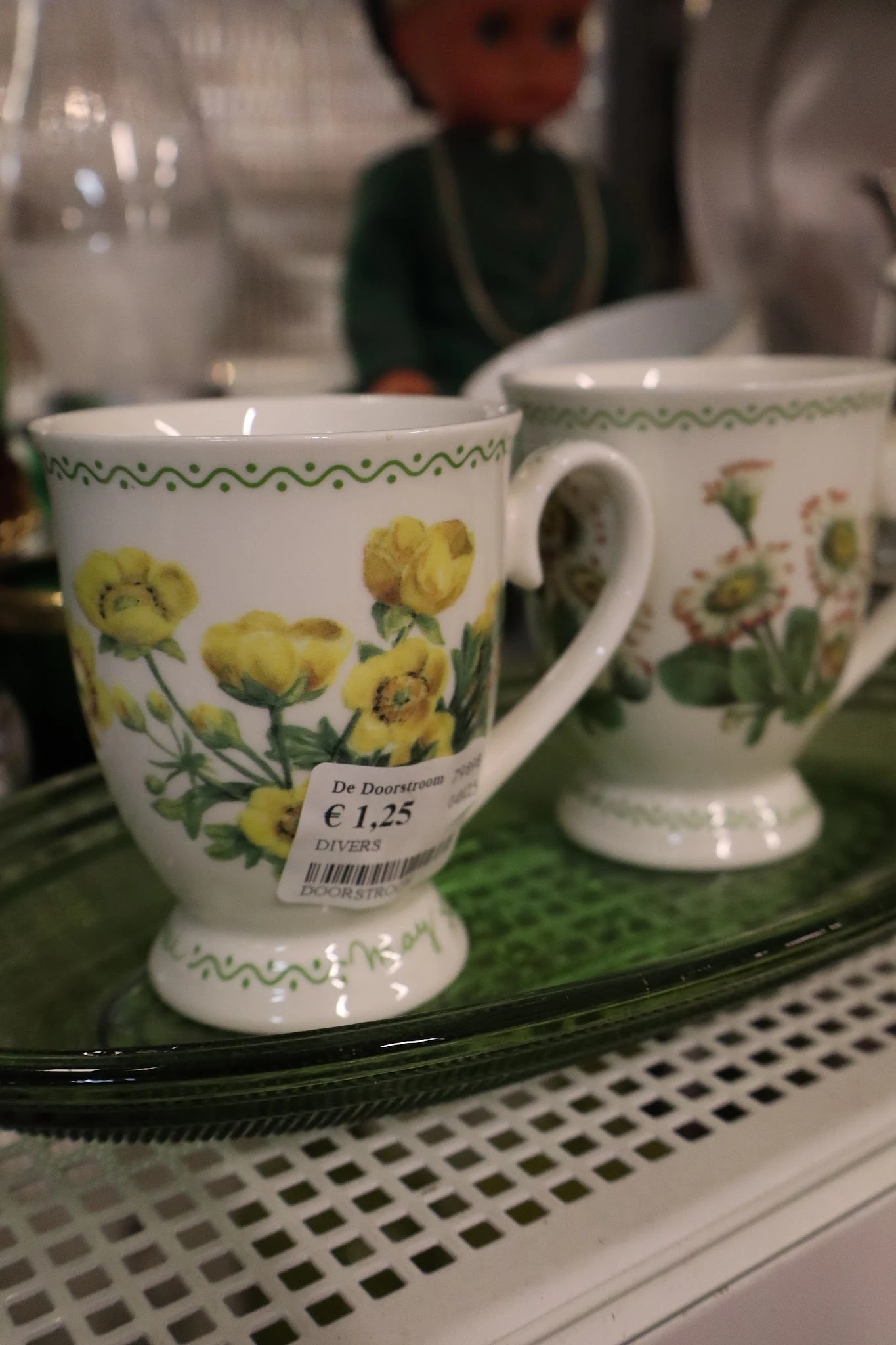 Witte porseleinen mok met gele bloemenprint en groene decoratieve rand, prijskaartje € 1,25