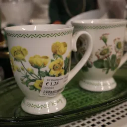 Witte porseleinen mok met gele bloemenprint en groene decoratieve rand, prijskaartje € 1,25