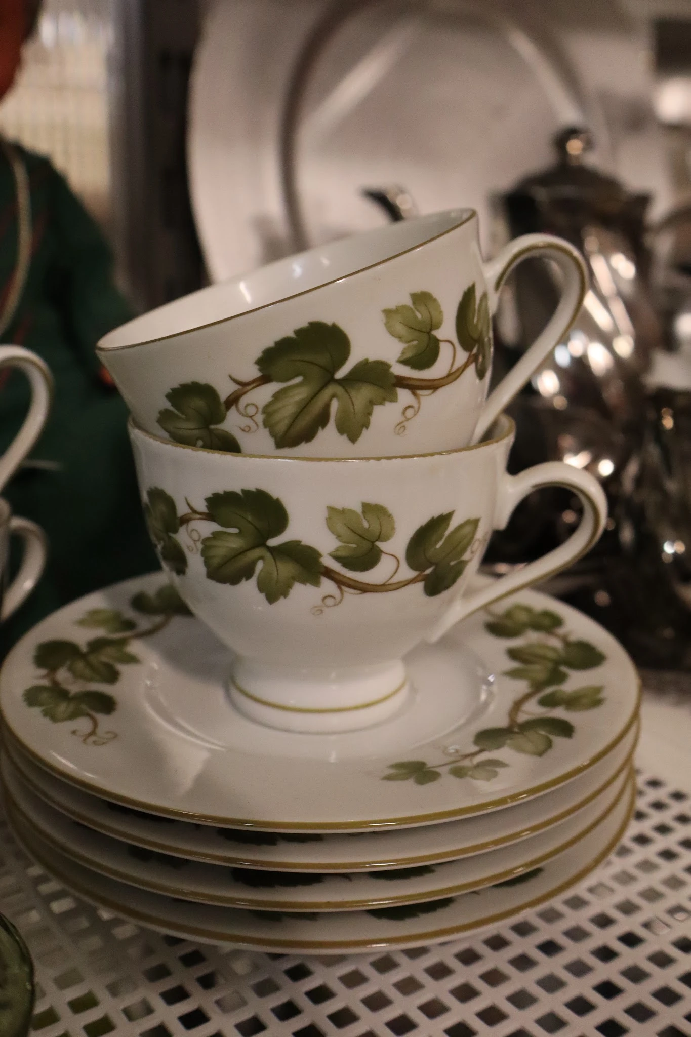 Twee gestapelde porseleinenen kopjes met groene druivenrank-decoratie op schotel