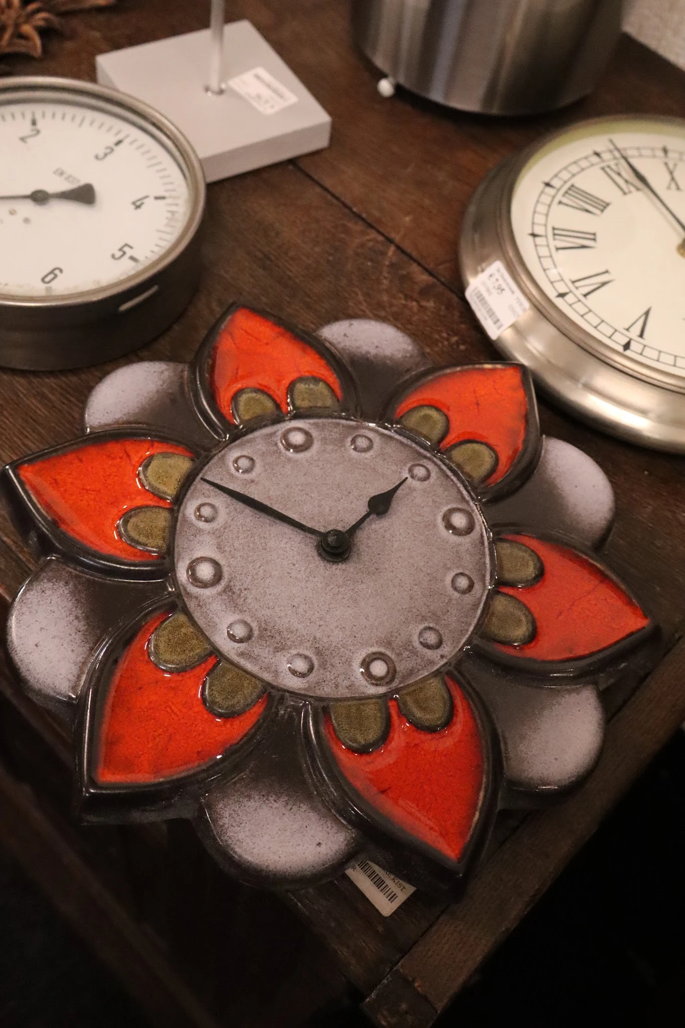 Close-up van een decoratieve bloemvormige klok met rode en witte details en metalen wijzers