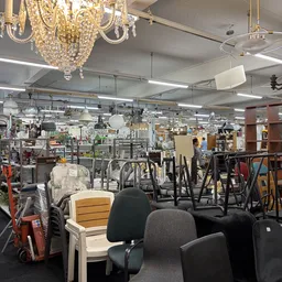 Winkelvloer met diverse tweedehands meubels en huishoudartikelen, waaronder stoelen, lampen en decoratie