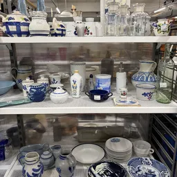 Glazen kastje met blauw-wit porselein servies, kannen, schalen en decoratieve items uit het aanbod van de kringloopwinkel