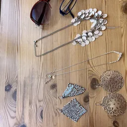 Uitgestalde sieraden en accessoires op houten tafel: zonnebril, parelketens, halskettingen en oorbellen