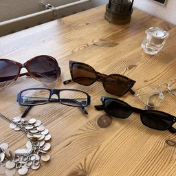 Uitgestalde tweedehands zonnebrillen en een zilveren ketting op een houten tafel