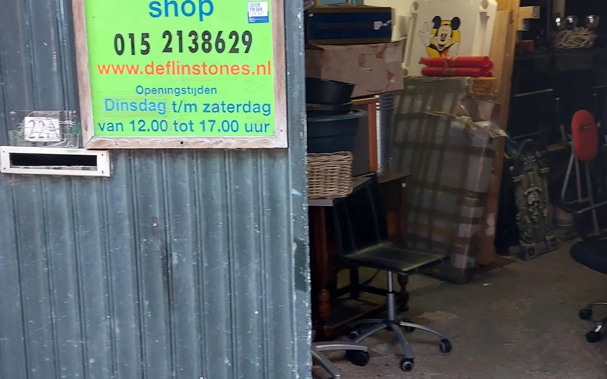 Winkelgevel met groen bord 'Second hand shop' met telefoonnummer en website, ingang met uitgestalde tweedehandsartikelen zich