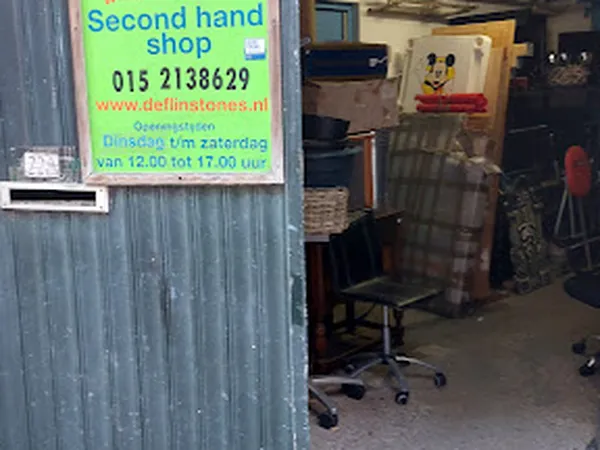 Groene bord 'Second hand shop' met telefoonnummer op grijze metalen deur, winkelraam met spullen zichtbaar