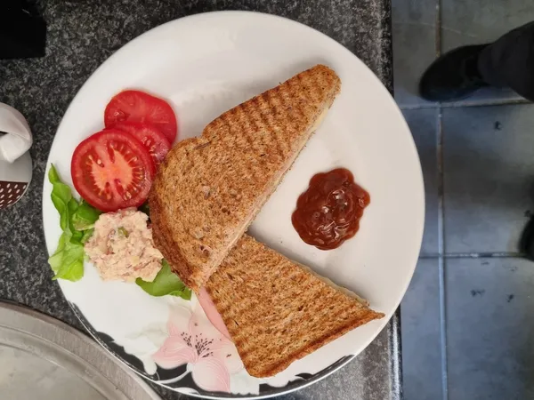 Bord met twee toastjes, tomatenplakken, ham, salade en sauzen.